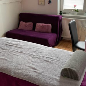 Eine Massageliege mit Decke, Handtuch, Kissen und Knierolle steht im Behandlungsraum von Miriam Georg